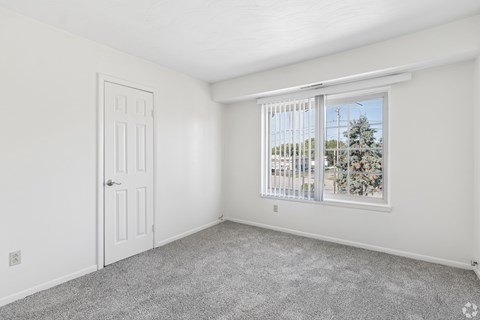 A room with a door and a window with a view of a tree.