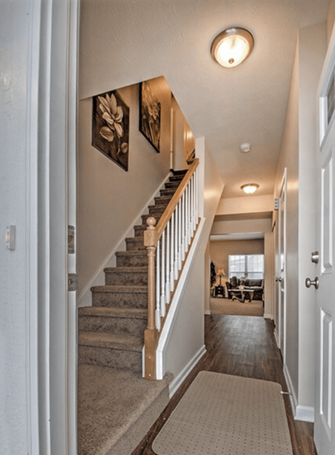 A hallway with a staircase and a rug on the floor.