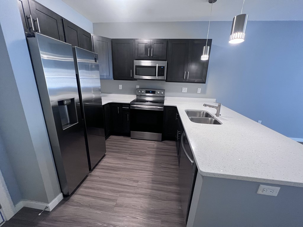 A modern kitchen with a stainless steel refrigerator and black cabinets.
