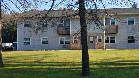 an apartment building with a lawn and trees in front of it