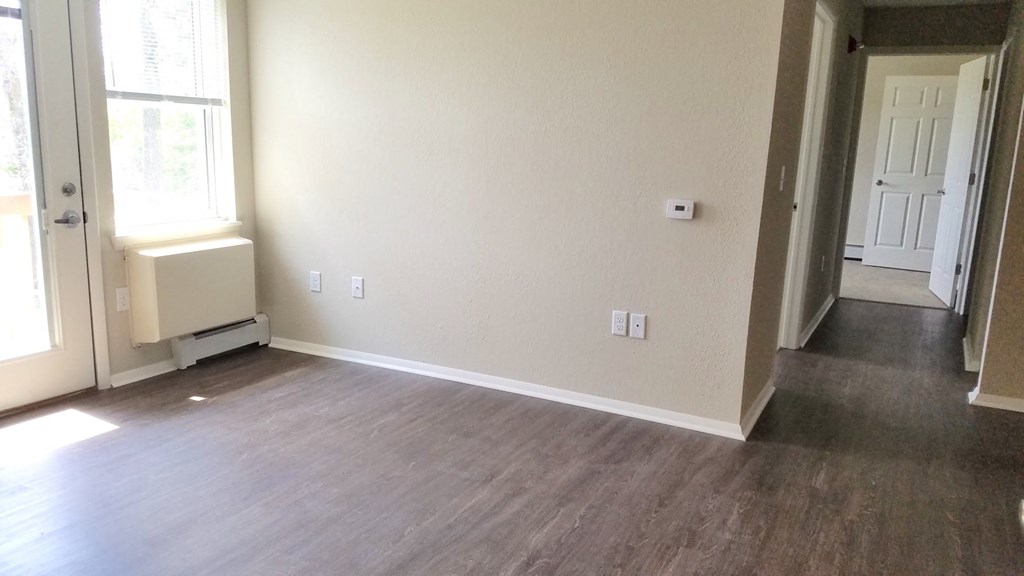 an empty living room with wood flooring and a white wall