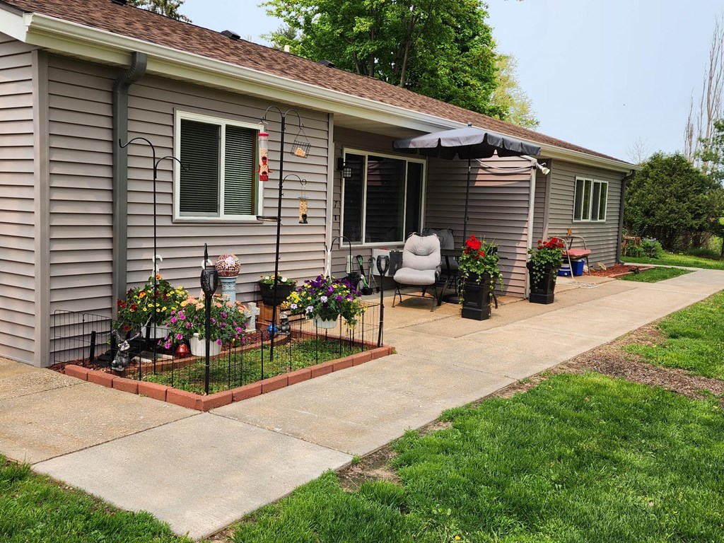 a home with a concrete walkway leading to a patio with an umbrella and chairs