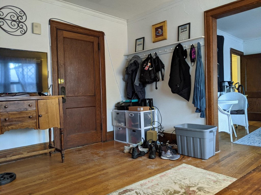 A room with a wooden floor and a white wall with a coat rack and a white chair.