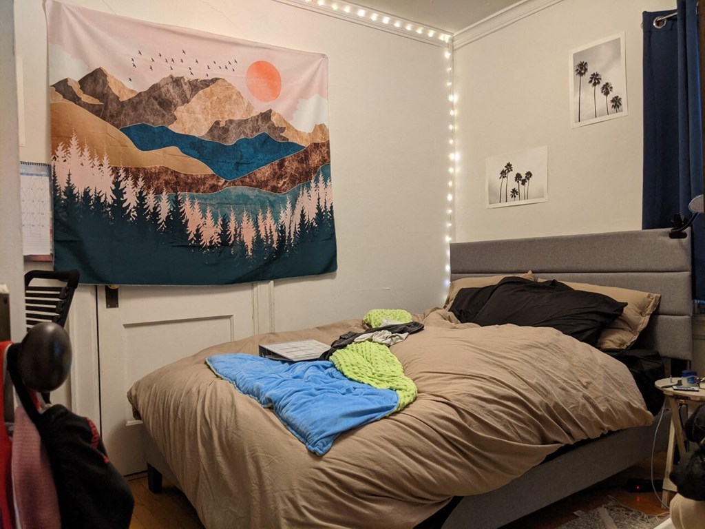 A bedroom with a bed, a blanket, a backpack, and a poster on the wall.