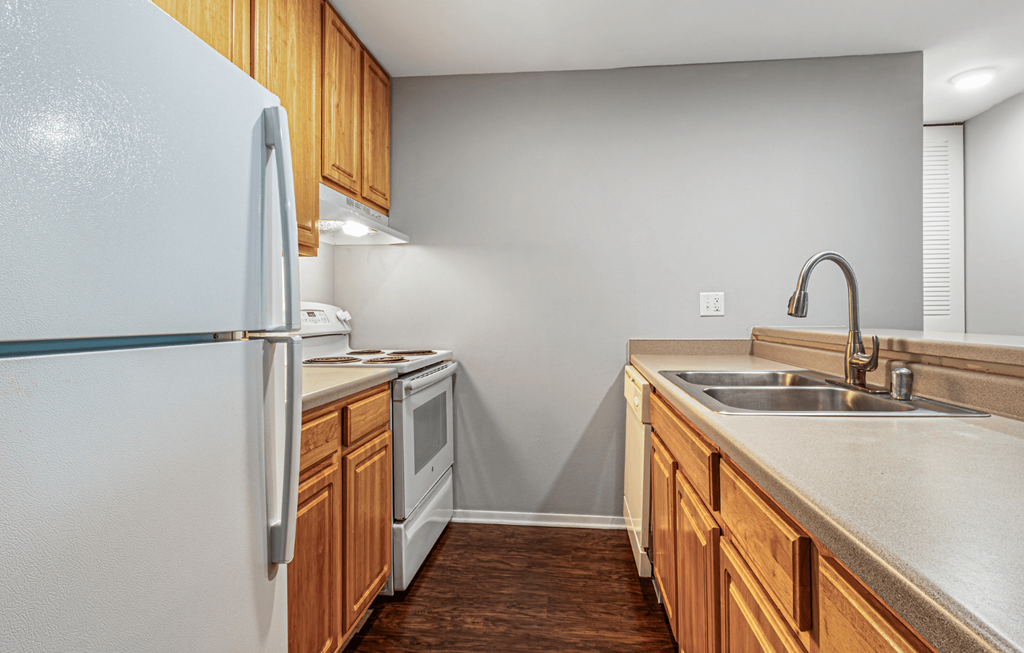 A kitchen with a white refrigerator, wooden cabinets, and a stainless steel sink.