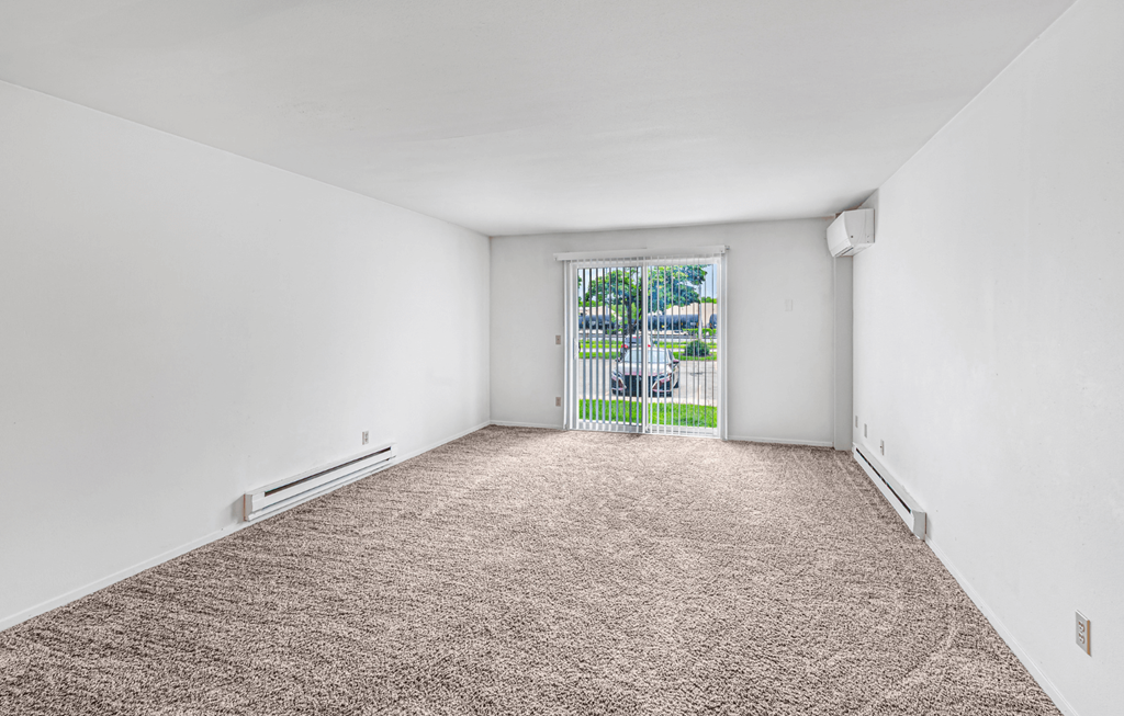 A room with a carpeted floor and a window with a view of a fence and trees.