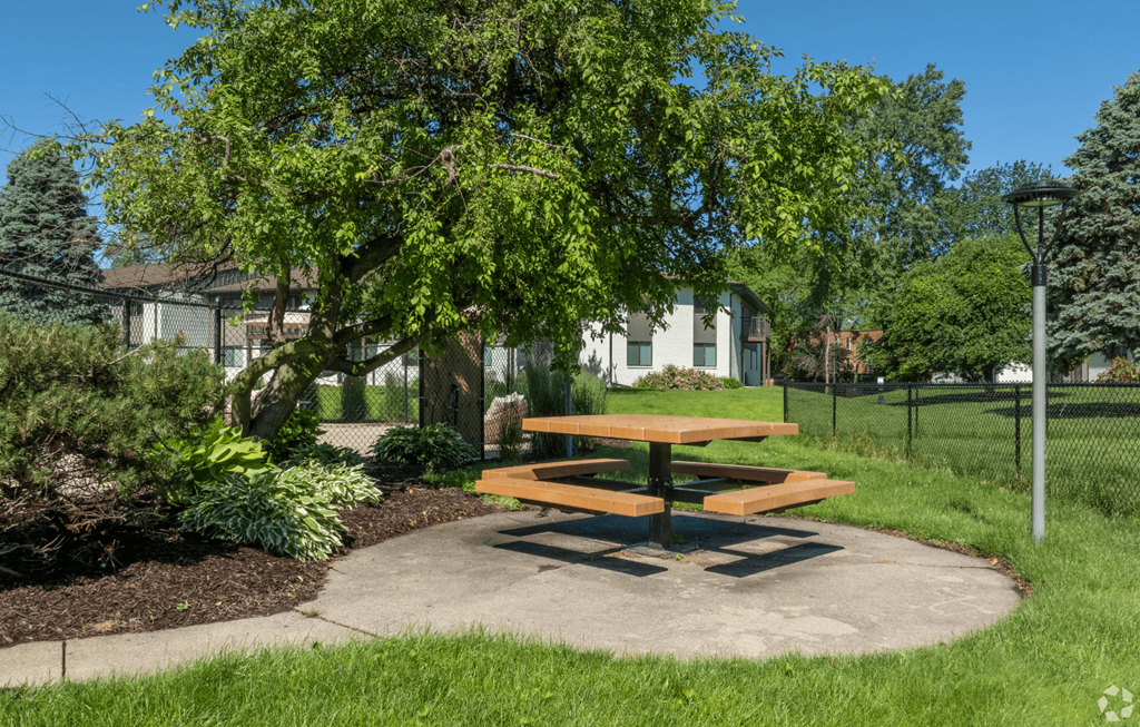 A picnic table is surrounded by greenery in a sunny park.
