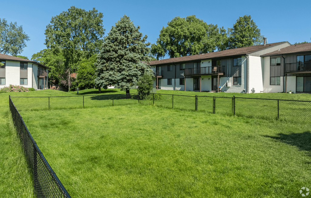 A grassy field with a fence and apartment buildings in the background.