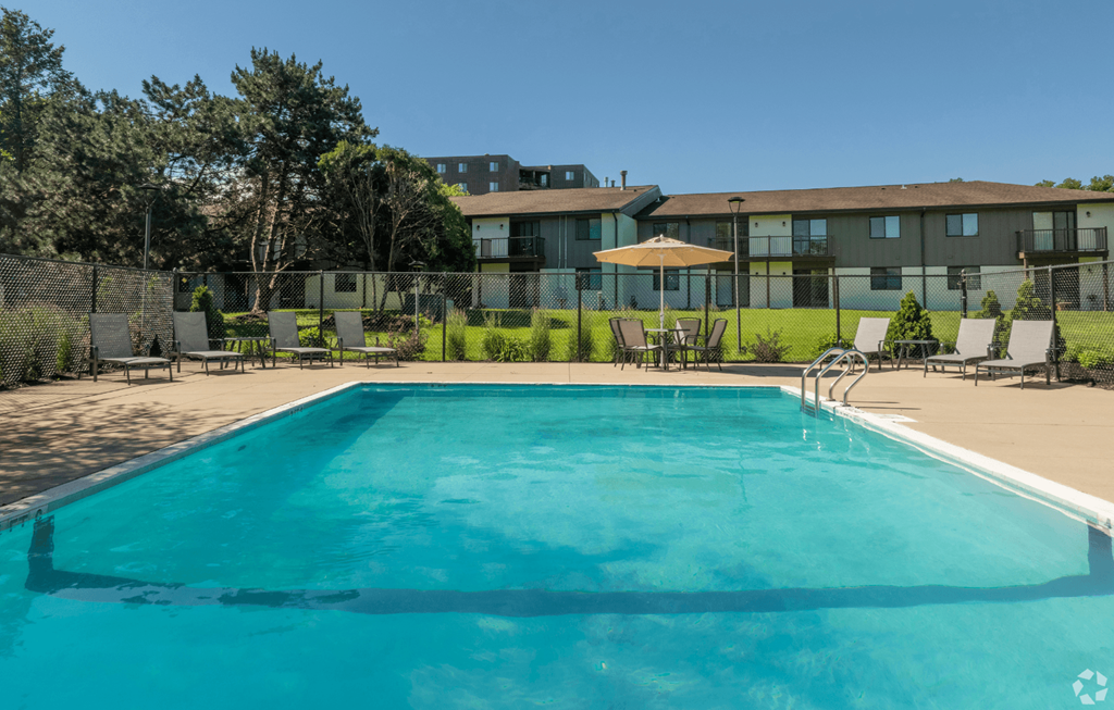 A large swimming pool in front of a building with a lawn and trees in the background.
