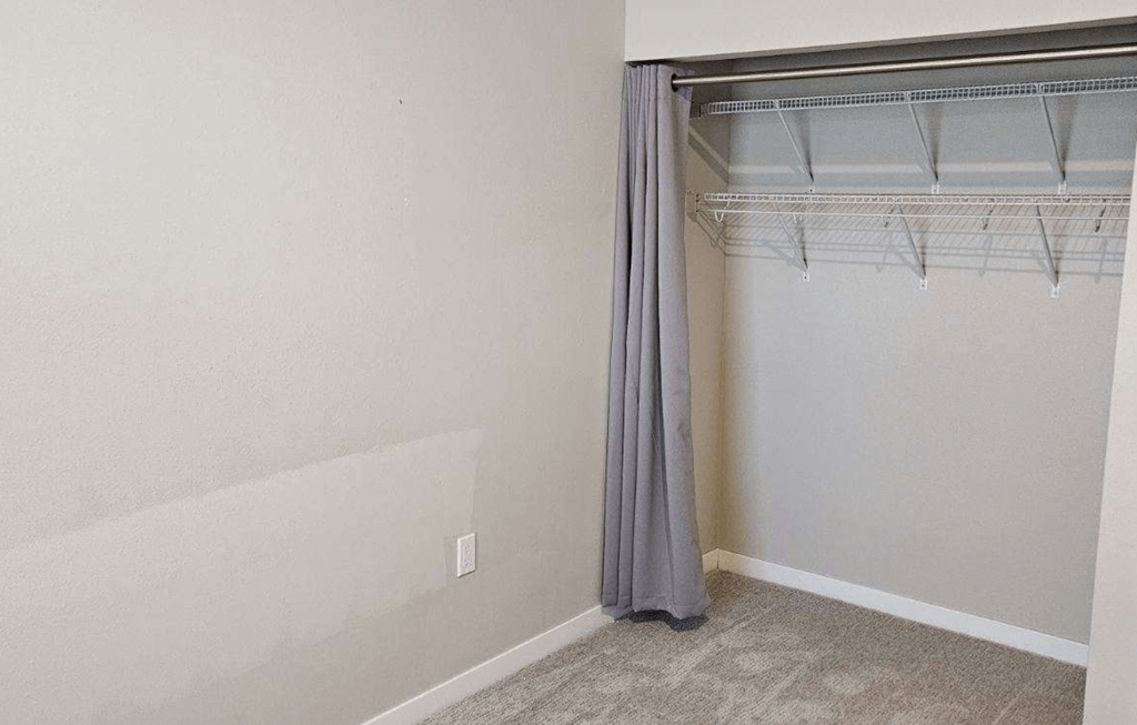 an empty bedroom with a closet with a curtain and a hanger