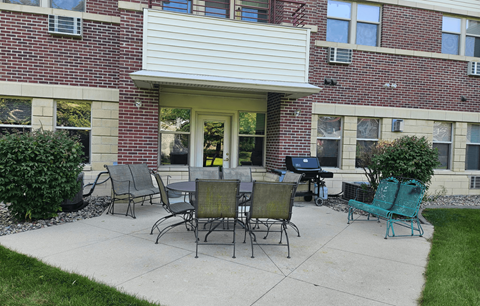 A patio with a table and chairs in front of a brick building.