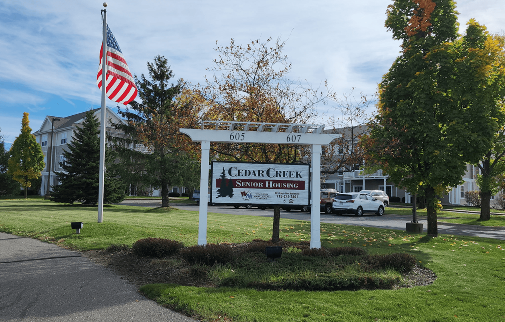 A sign for Cedar Creek Senior Housing stands in front of a building.