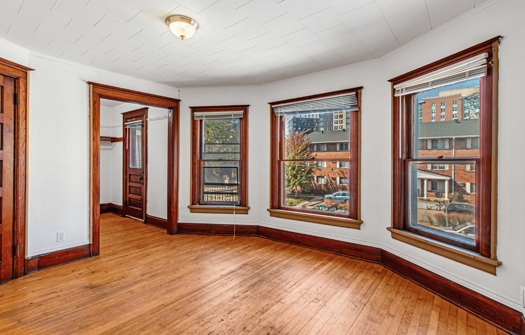 A room with a white ceiling and wooden floors with three windows.