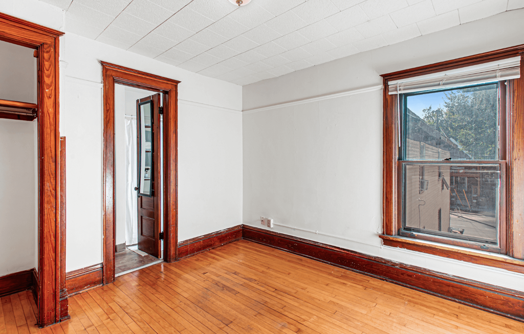 A room with a wooden floor and a window showing a building outside.