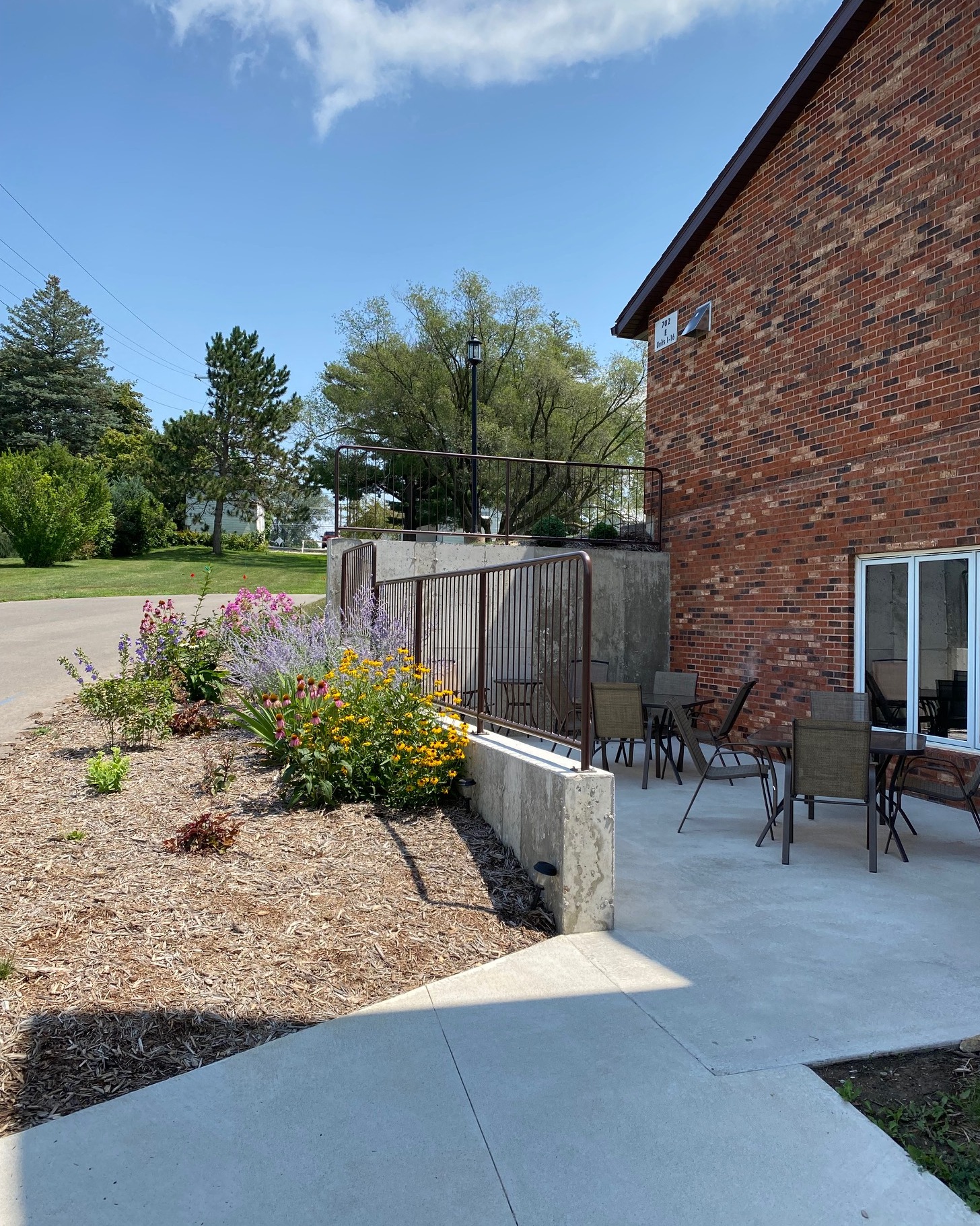 A patio with a table and chairs is surrounded by a flower bed and a brick building.