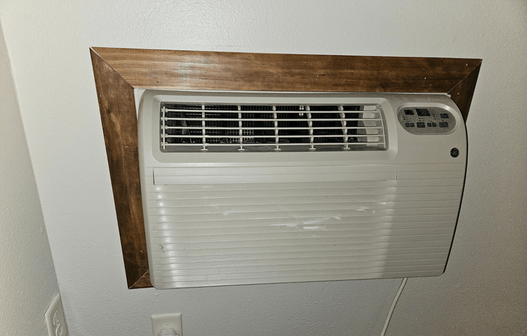 an air conditioning unit mounted on a wall with a wooden shelf above it