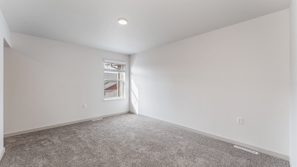 A large empty room with a carpeted floor and a window.
