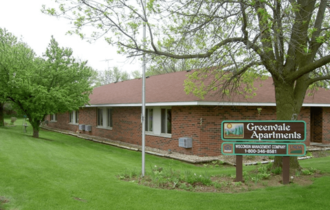 A sign for Greenwale Apartments is in front of a brick building.