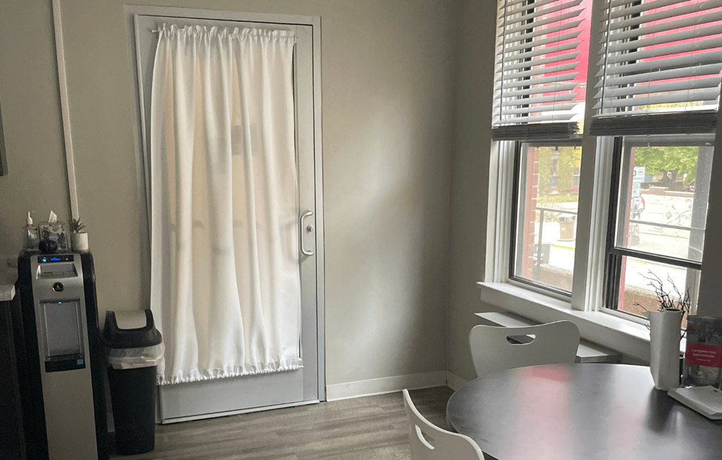 A room with a table, chairs, and a window with red blinds.
