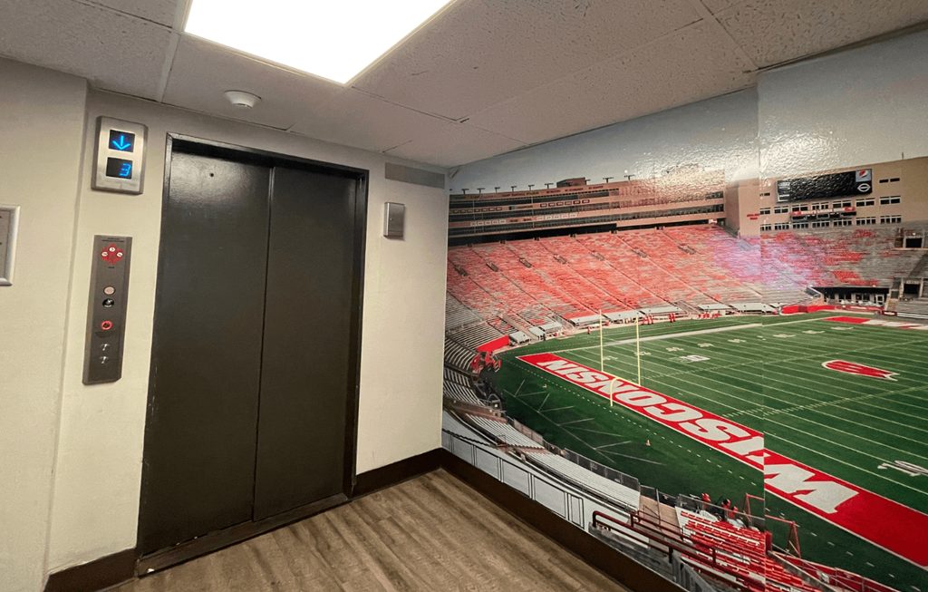 A wall mural of a football stadium is painted on the wall in a room with a black door.