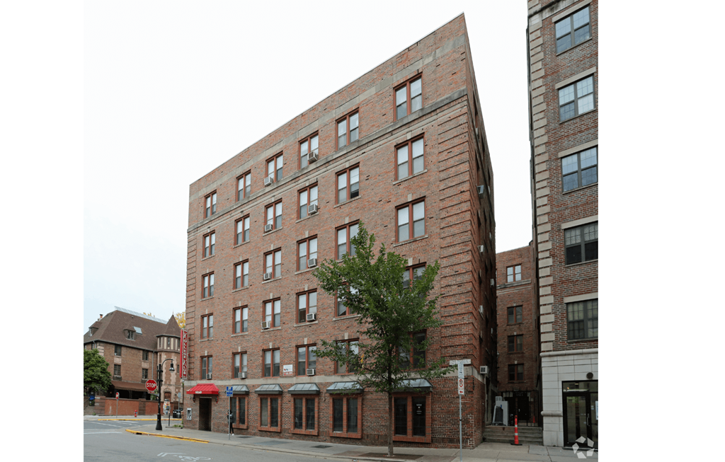 A tall red brick building with many windows stands on a street corner.