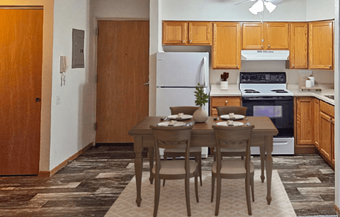 A kitchen with a table set for two with a refrigerator and oven in the background.