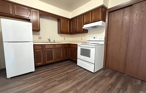 A white refrigerator stands in a kitchen with wooden cabinets and a white stove.