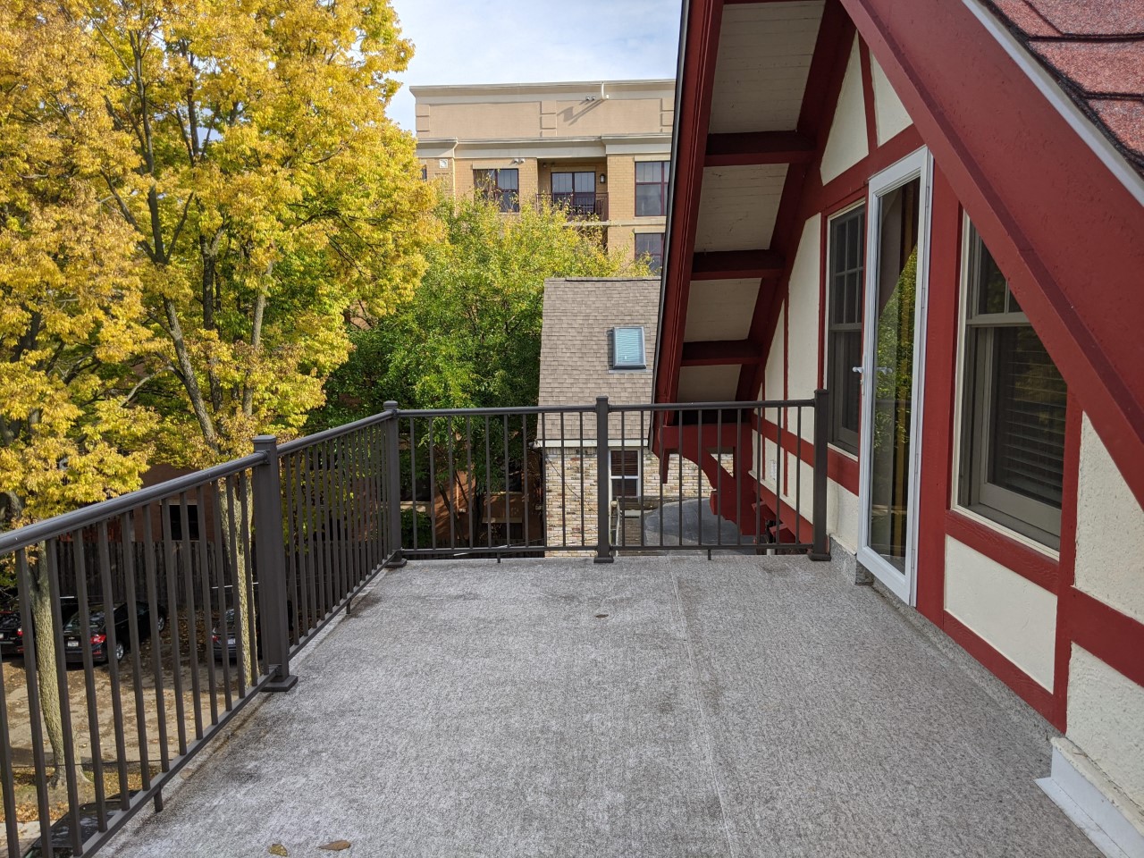 A balcony with a black railing and a red and white building in the background.