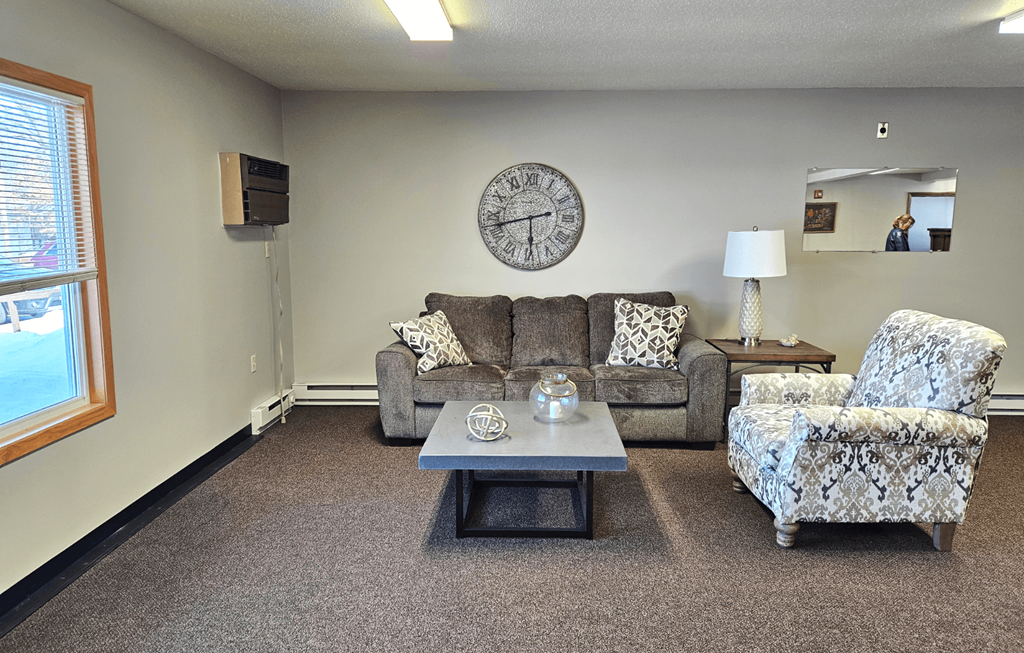 a living room with a couch a chair a coffee table and a clock on the wall
