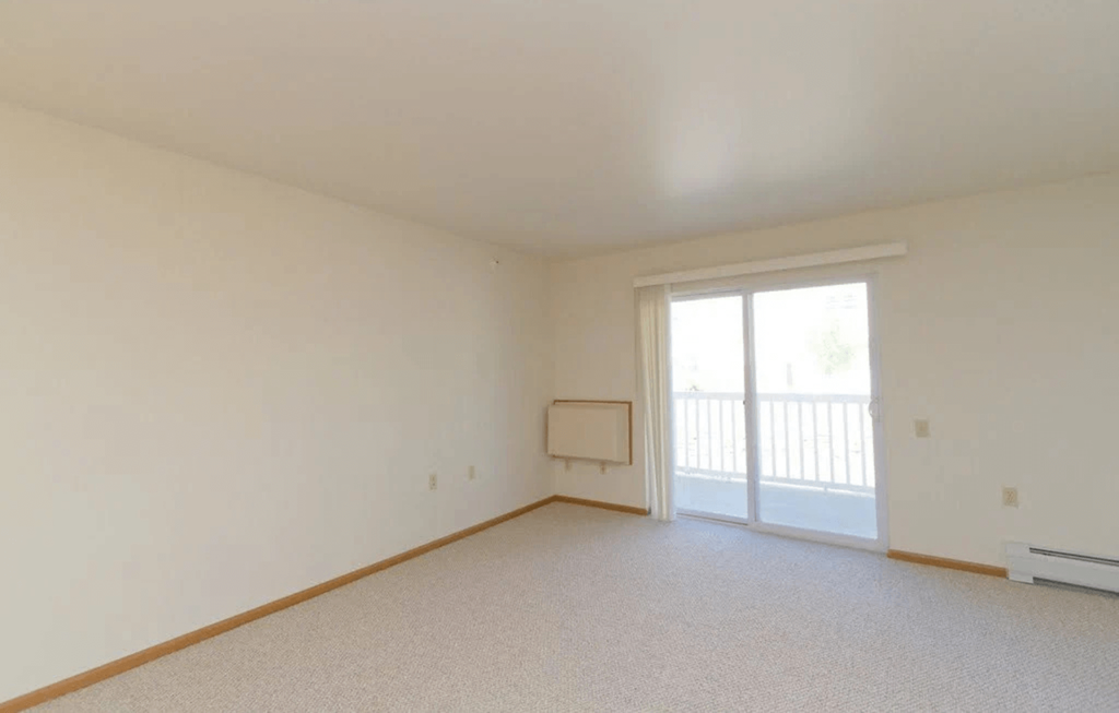 an empty living room with a sliding glass door to a balcony