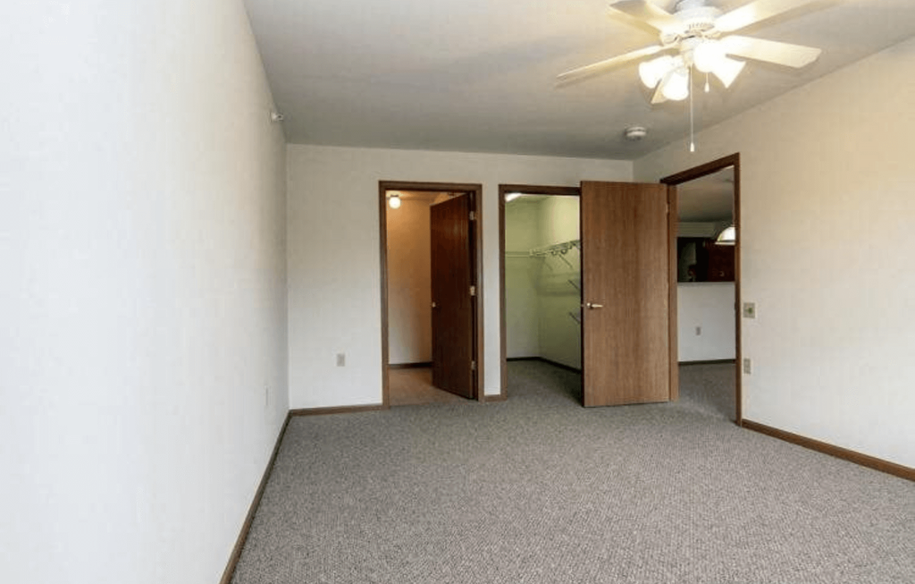 an empty living room with a ceiling fan and a closet