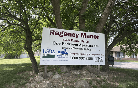 A sign for Regency Manor Apartments is displayed in front of some trees.