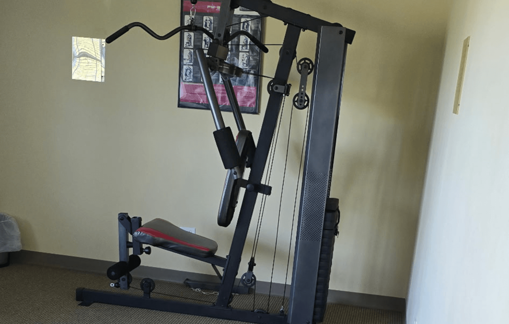 A black home gym machine with a red seat and a grey handle.