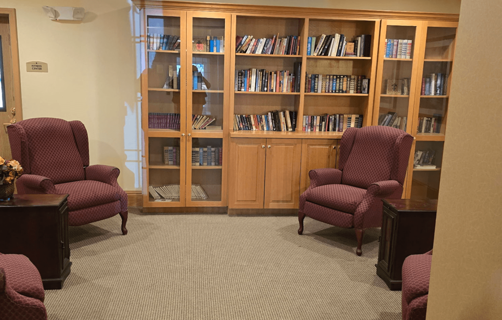 A room with a bookcase and two chairs.
