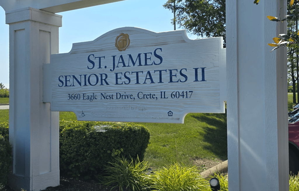 A sign for St. James Senior Estates II stands in front of a green lawn.