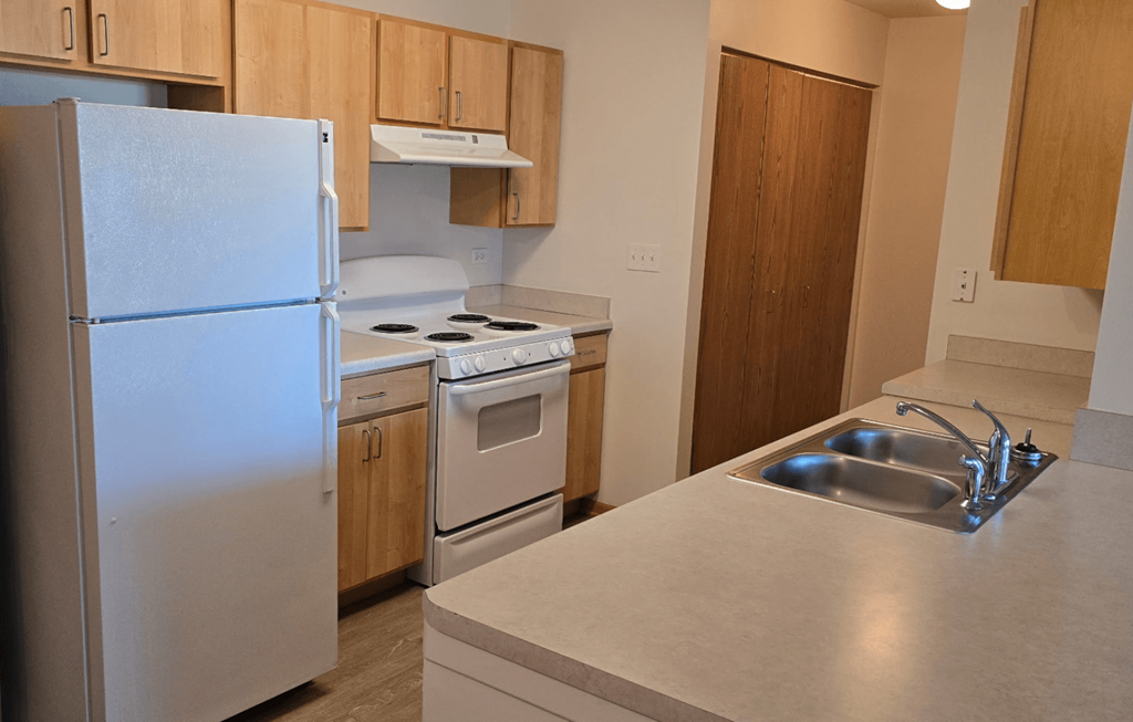 A kitchen with a white fridge, stove, and sink.