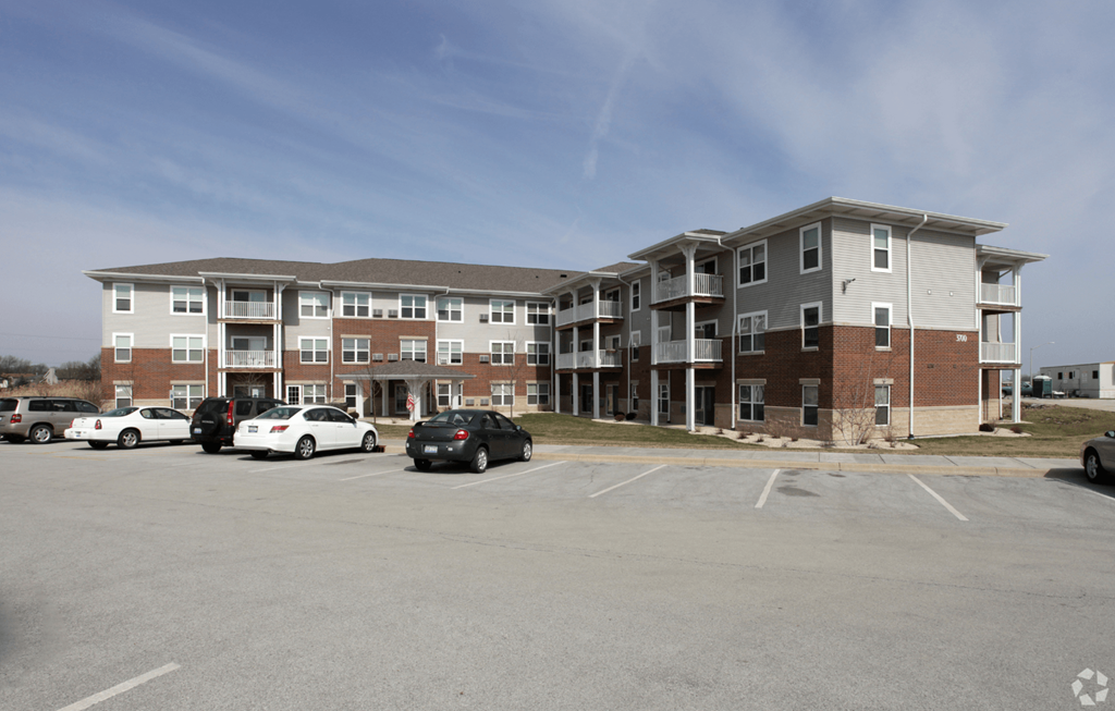 A parking lot in front of a multi-story apartment building with cars parked.