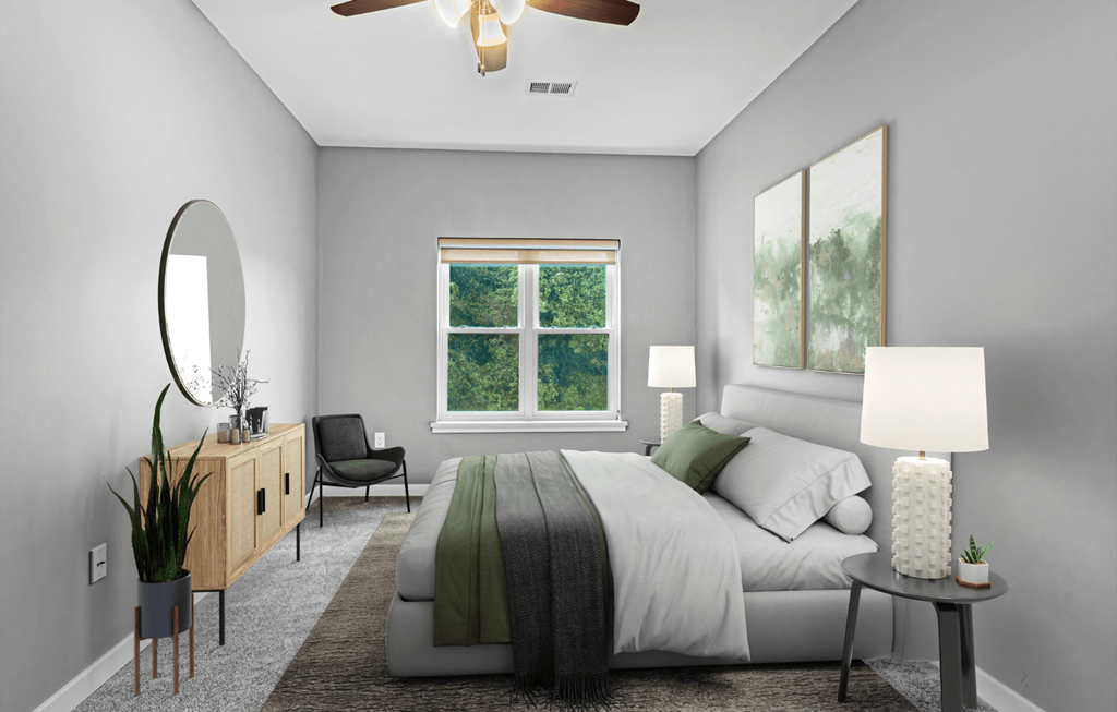 A bedroom with a bed, a chair, a side table, a mirror, and a ceiling fan.