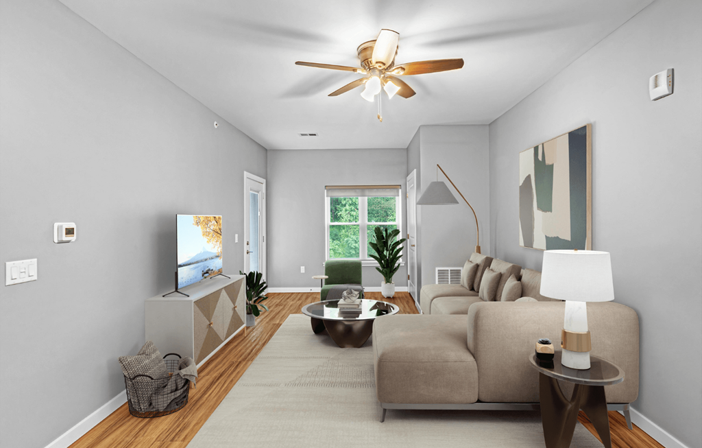 A living room with a beige couch, a coffee table, a television, and a ceiling fan.