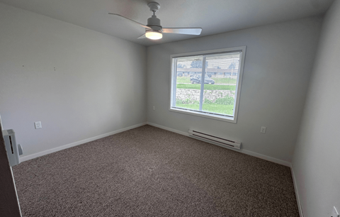 A room with a ceiling fan and a window overlooking a parking lot.