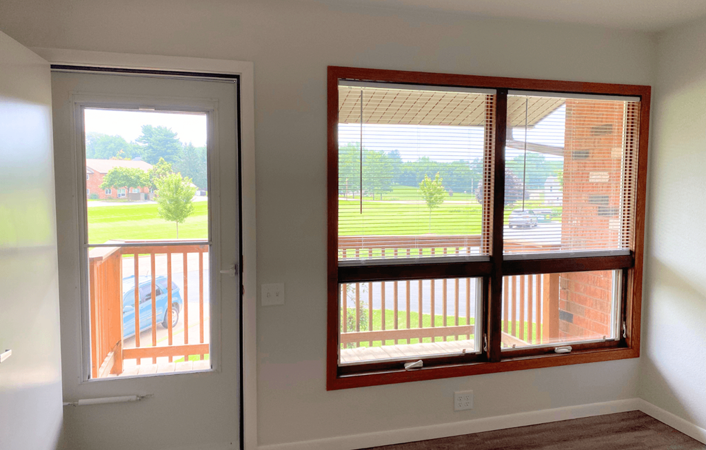 A room with a view of a deck and a house through the window.