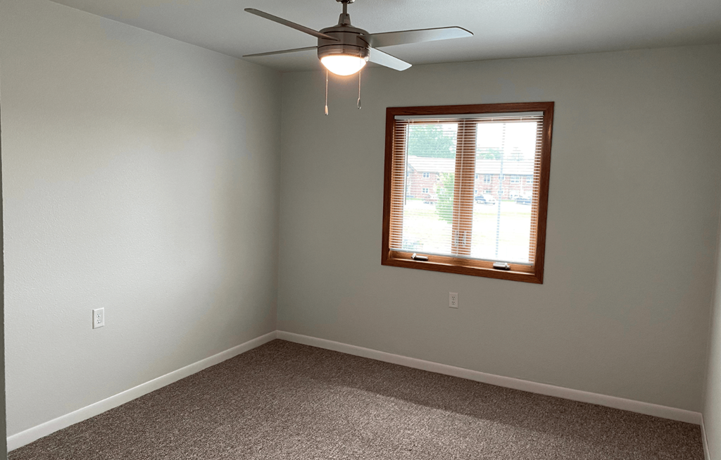A room with a ceiling fan and a window with blinds.