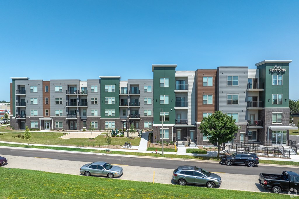 A row of modern apartment buildings with cars parked in front.