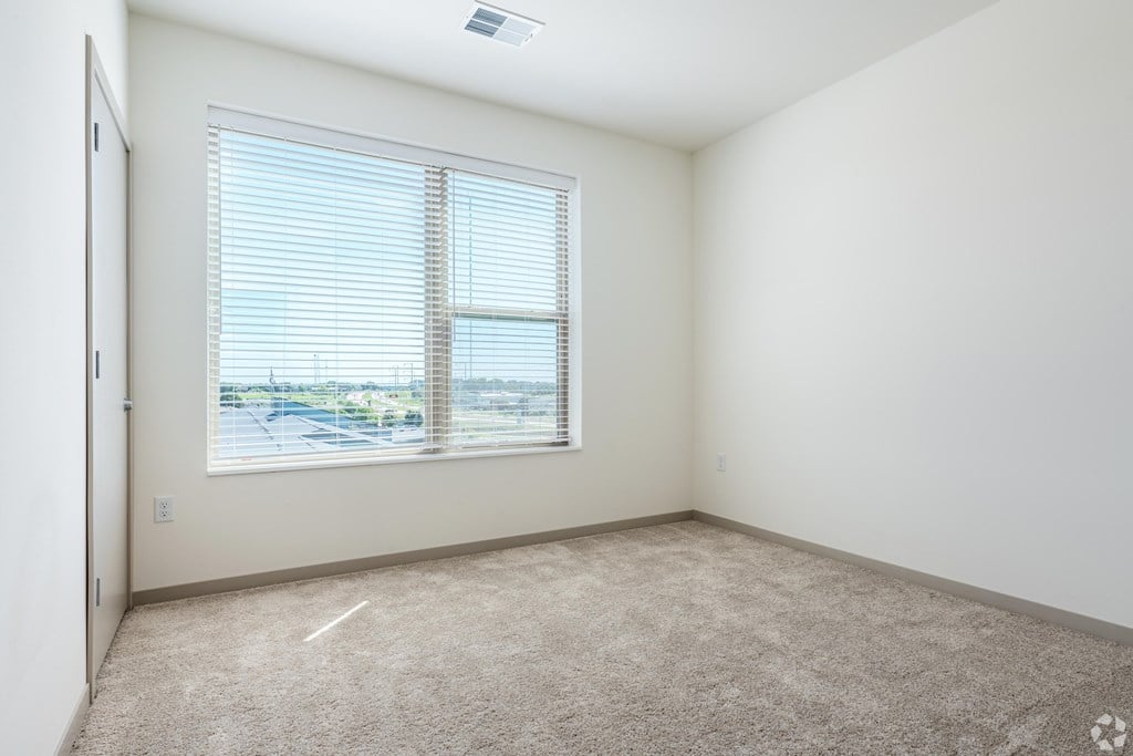 A room with a carpeted floor and a window with blinds.