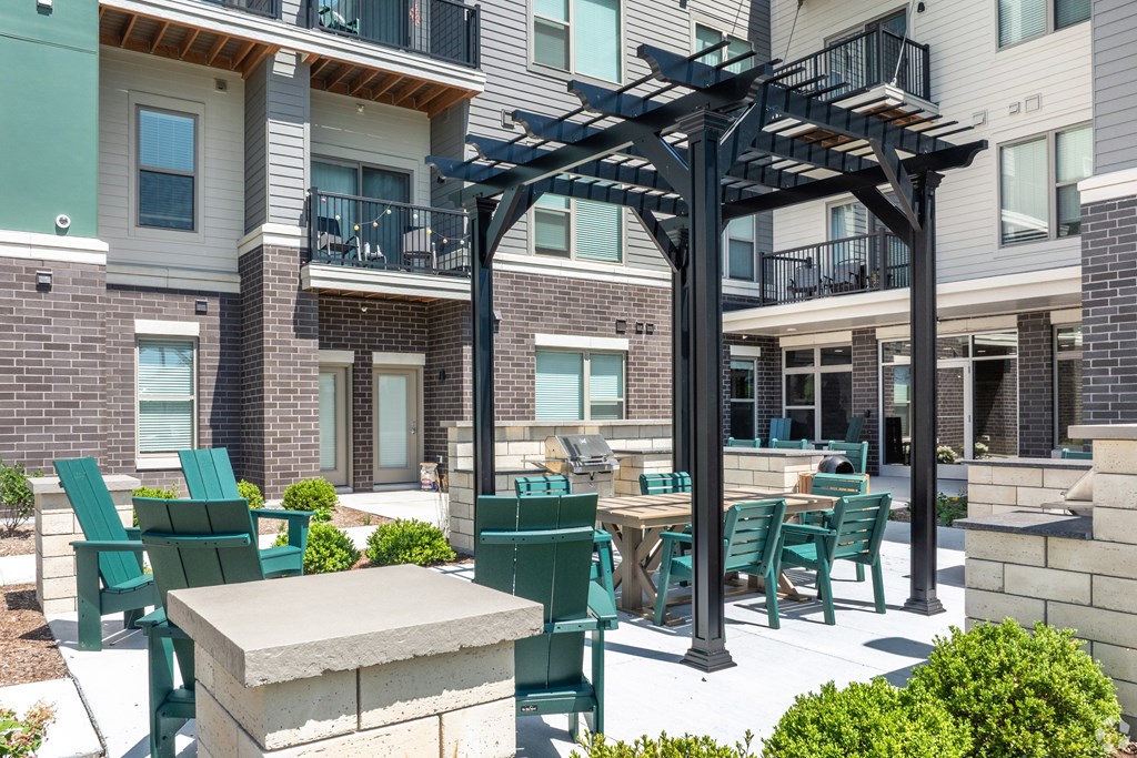 A patio with green chairs and a table is surrounded by apartment buildings.
