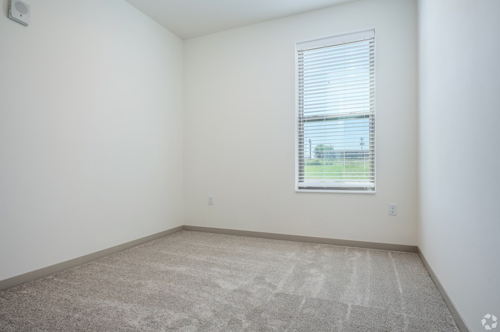 A room with a carpeted floor and a window with blinds.