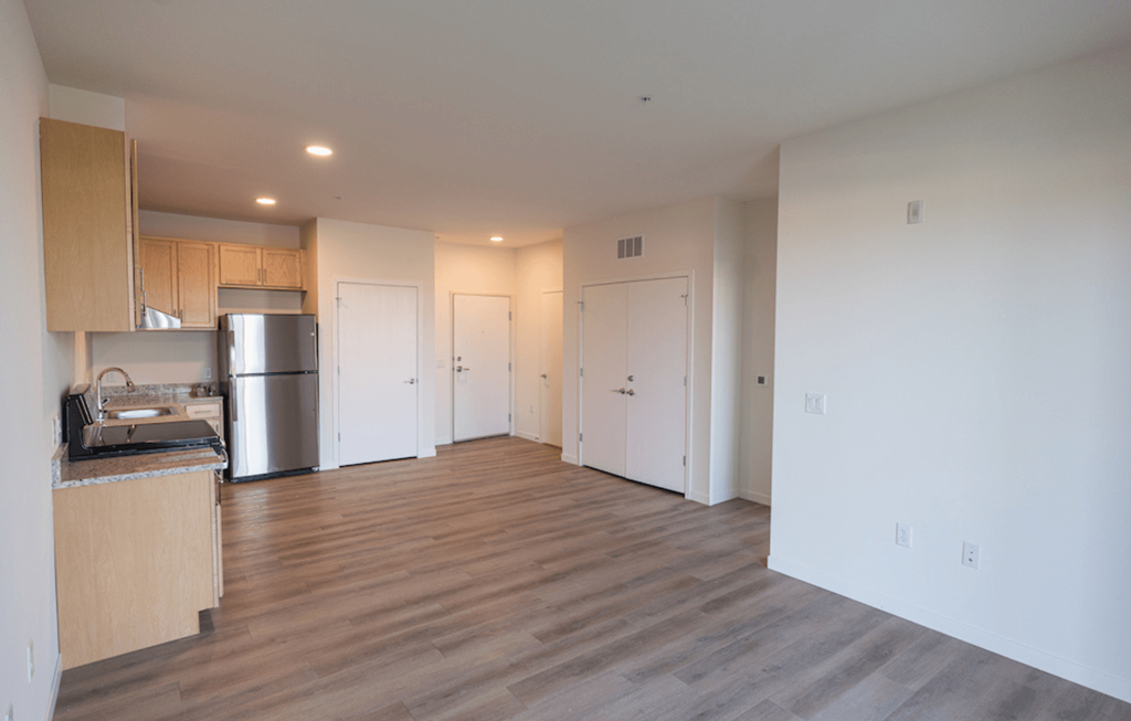 an empty living room and kitchen with wood floors and white walls