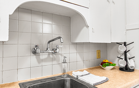 A kitchen sink with a bowl of fruit on the counter.