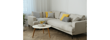 A grey couch with a yellow pillow and a small table with a vase of flowers on it.