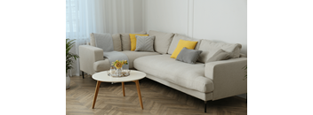 A grey couch with a yellow pillow and a small table with a vase of flowers on it.